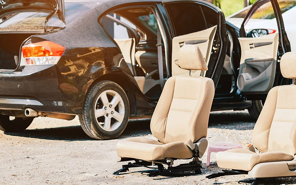 Technician removing car seat after unbolting and disconnecting wiring harness for headliner access